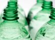 Several PET bottles stand in two rows, focusing on the bottle necks and openings. The bottles contain a clear liquid. 