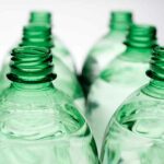 Several PET bottles stand in two rows, focusing on the bottle necks and openings. The bottles contain a clear liquid. 