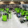Produktionsanläggning med flera ljusgröna formsprutningsmaskiner i industriell miljö.