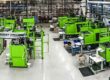 Production facility with multiple light green injection moulding machines in an industrial environment.