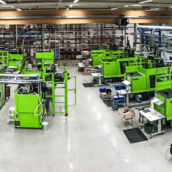 Formsprutning_centramec_600px Produktionsanläggning med flera ljusgröna formsprutningsmaskiner i industriell miljö.