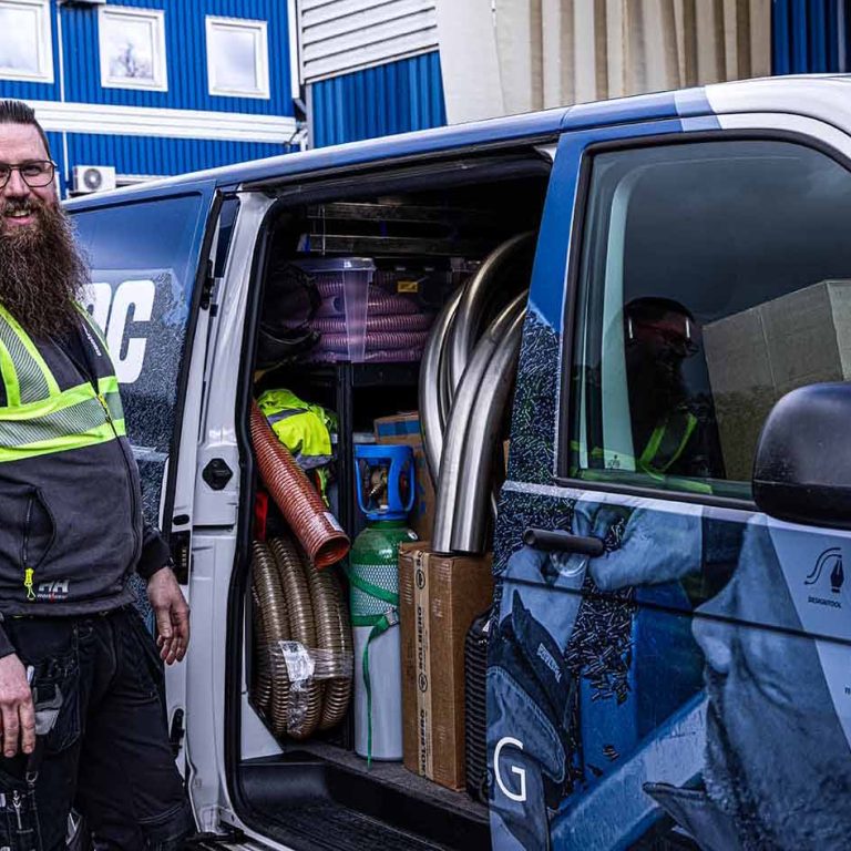 Mitarbeiter in Warnschutzjacke vor dem folierten Servicefahrzeug von Centramec. Die Seitentür ist geöffnet und man kann Installationszubehör, Spiralrohre und Rohrbögen sehen.