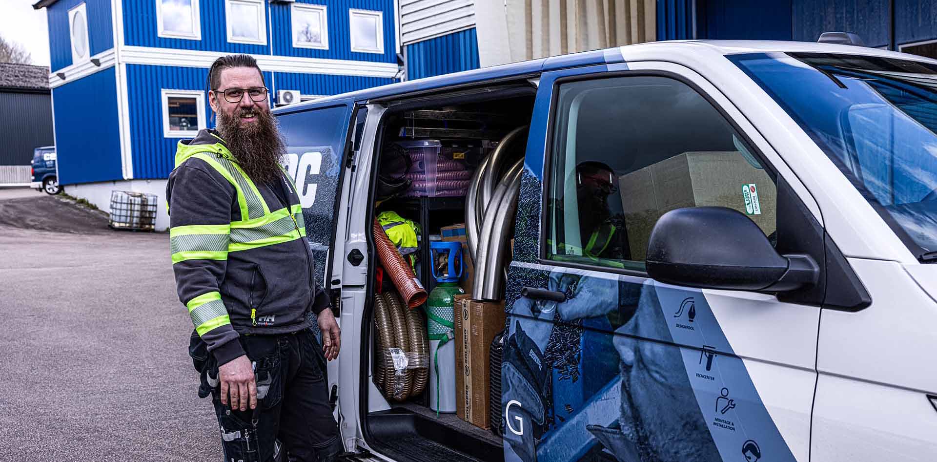 Service_Centramec Medarbetare i varseljacka utanför Centramecs folierade servicebil, sidodörren är öppen och man ser installationsdetaljer, spirorör och rörböjar.