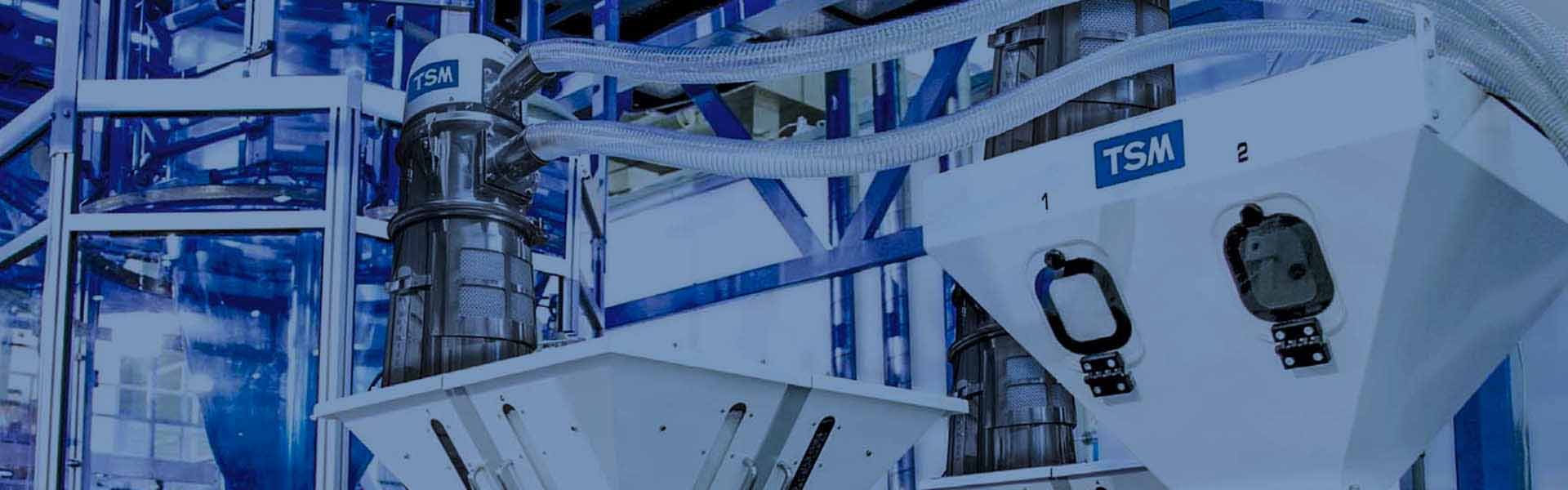 Två TSM batchblandare i industriell miljö, blått stallage, en styrenhet och anslutna slangar.